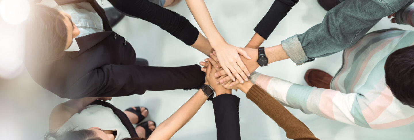 Group of diverse individuals standing in a circle with hands joined together in the center.