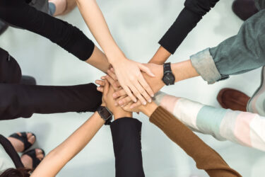 Group of diverse individuals standing in a circle with hands joined together in the center.