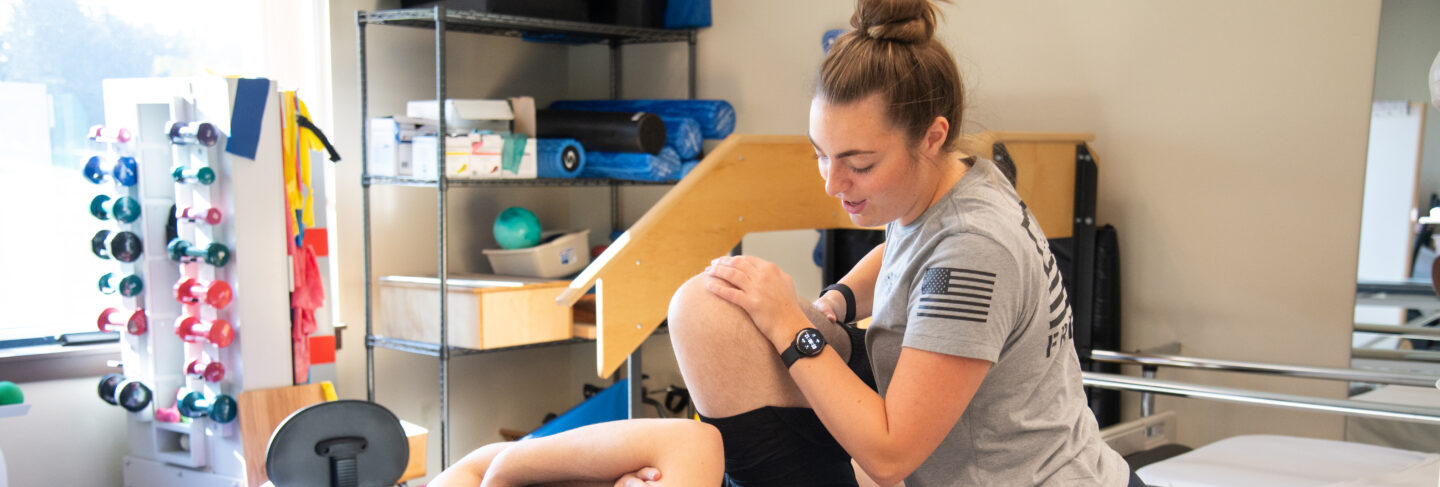 Physical therapy student practicing knee exercises on a patient in a training room.