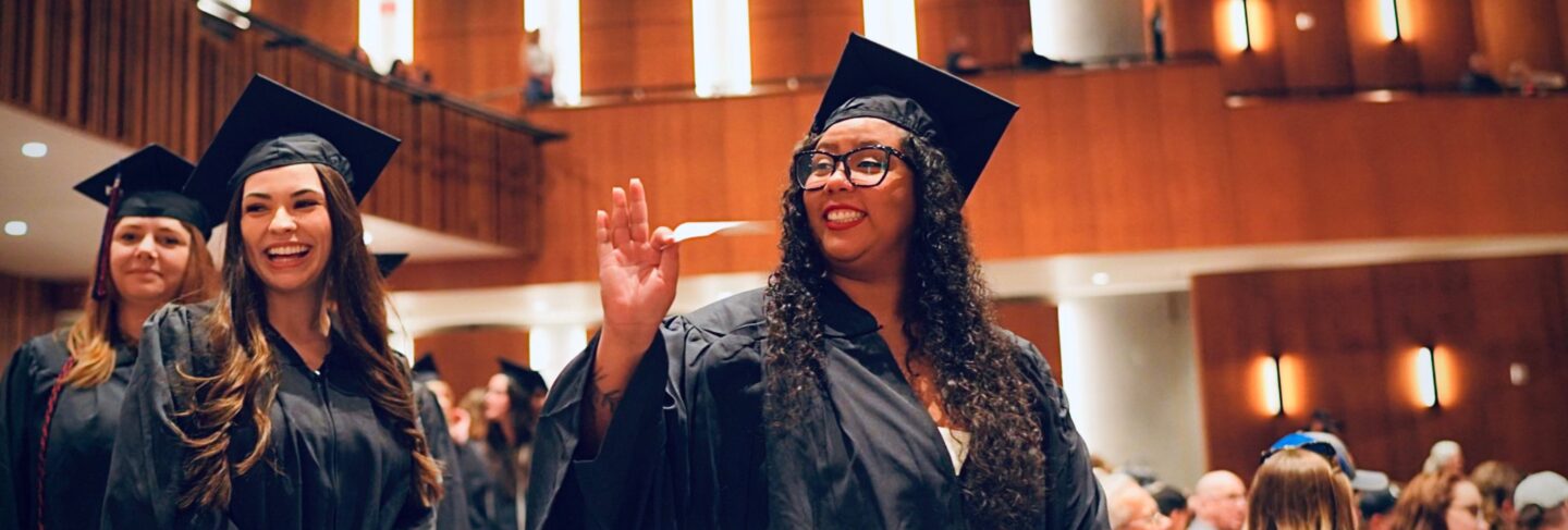 student at graduation smiling and waving to the crowd.