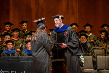 Graduating student receiving diploma on stage from faculty member during Flathead Valley Community College commencement ceremony.