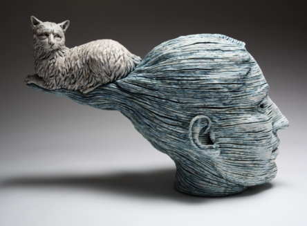 Adrian Arleo piece. Art piece is a stone-like head with pulled back hair thats twisted to be pulled back straight and with cat sitting on top twisted hair