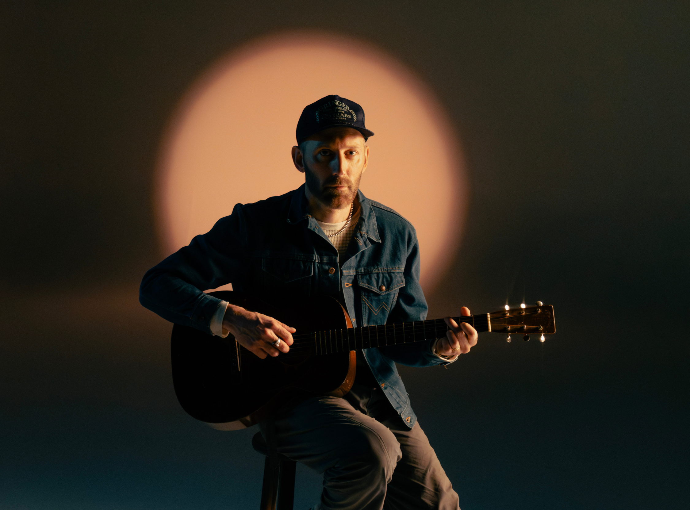 Mat Kearney holding guitar sitting on a stool